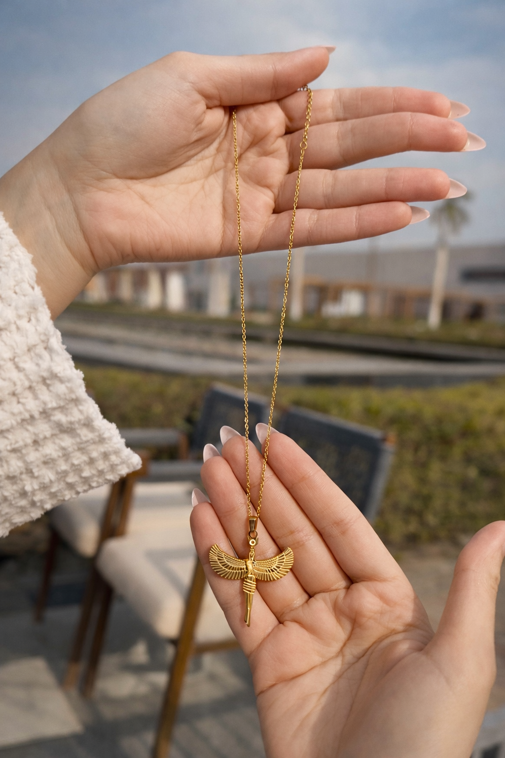 Gold necklace with a pendant held in hands outdoors