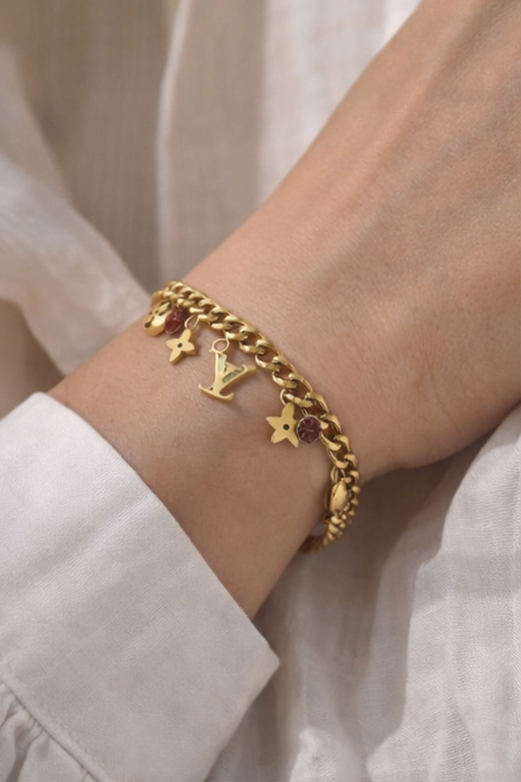 Gold bracelet with charms on a wrist against a neutral background