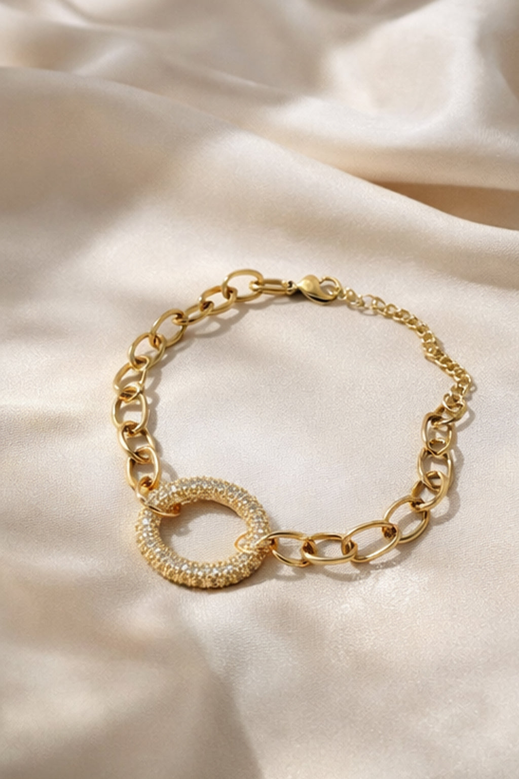 Gold chain bracelet with a circular design on a beige fabric background