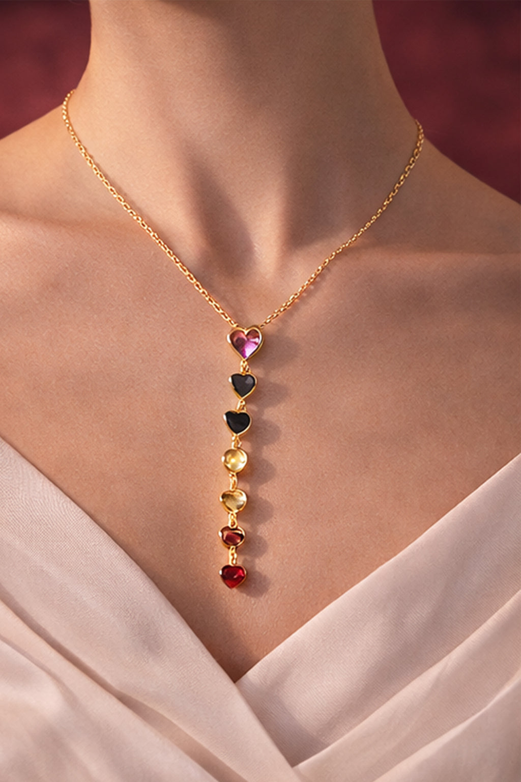Gold necklace with colorful heart-shaped pendants on a person wearing a white dress.